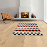 Wohnzimmer mit Kamin, braunem Sessel, Holzfußboden und buntem geometrischem Teppich.