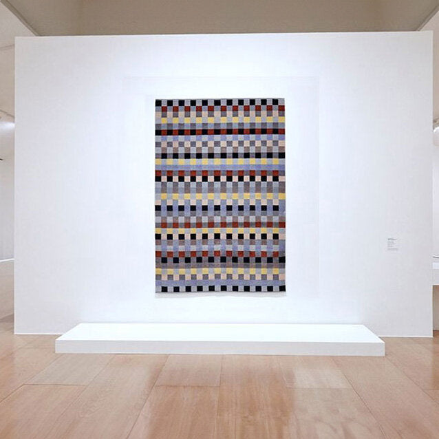 Hängendes Wandbild mit geometrischem Muster aus bunten Quadraten in einem Museum.