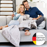 Ein lachendes Paar sitzt auf einem Sofa, die Frau ist schwanger, beide umarmen sich.