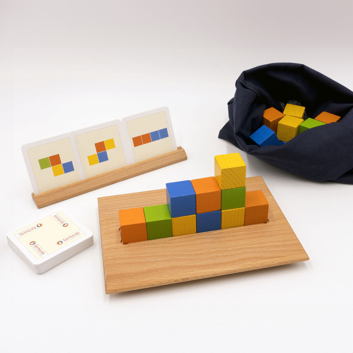 Bunte Holzbausteine auf einem Holzbrett, Spielkarten, ein Beutel mit weiteren Bausteinen, alles auf weißem Hintergrund.