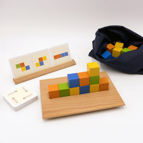 Bunte Holzbausteine auf einem Holzbrett, Spielkarten, ein Beutel mit weiteren Bausteinen, alles auf weißem Hintergrund.