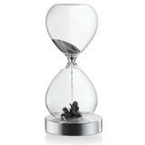 Sanduhr mit schwarzen Sand und Dekoration am Boden, auf silbernem Sockel.