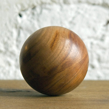 Runder, glatter Holzball mit sichtbarer Maserung vor weißer Wand.