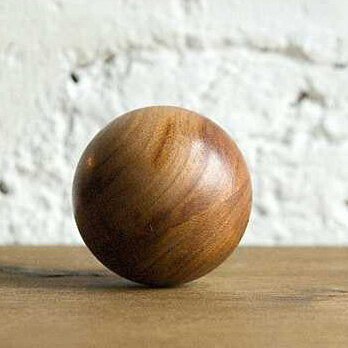 Ein runde, braune Holz-Kugel auf einer Holzfläche vor weißer Wand.