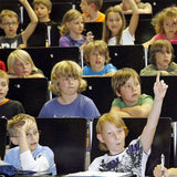 Kinder sitzen in einem Klassenzimmer, einige heben die Hand, andere schauen nach vorne.