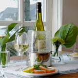 Weißwein, eine Flasche in einem Eisbehälter, Blumenvasen mit grünen Blättern, ein Teller mit Lachs und Zitronenscheiben.