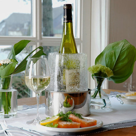 Weißwein, eine Flasche in einem Eisbehälter, Blumenvasen mit grünen Blättern, ein Teller mit Lachs und Zitronenscheiben.