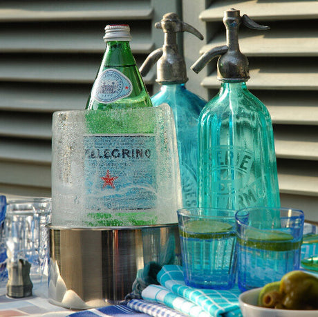 Bunte Glasflaschen, eine Flasche in einem Eisbehälter, zwei Gläser mit Zitronenscheiben, eine kleine Schale mit Oliven.