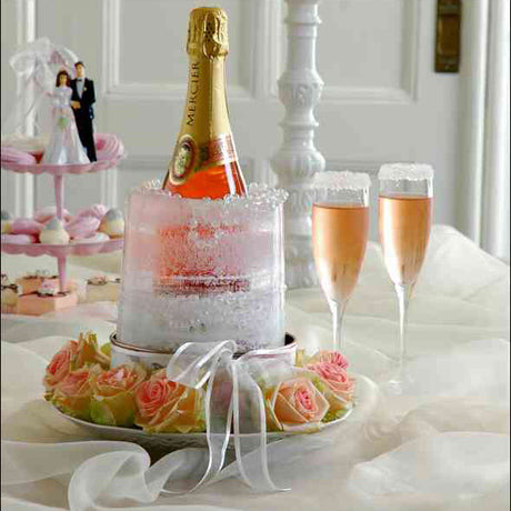 Flasche Champagner in Eis, zwei Gläser mit Rosé-Sekt, Blumen und Cupcakes auf einem festlich gedeckten Tisch.