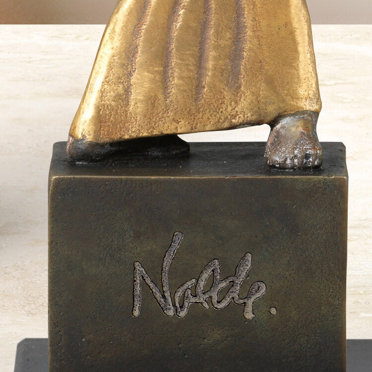 Skulptur mit goldener Robe, nur die Füße sichtbar, auf einem schwarzen Sockel mit der Unterschrift "Nolde".