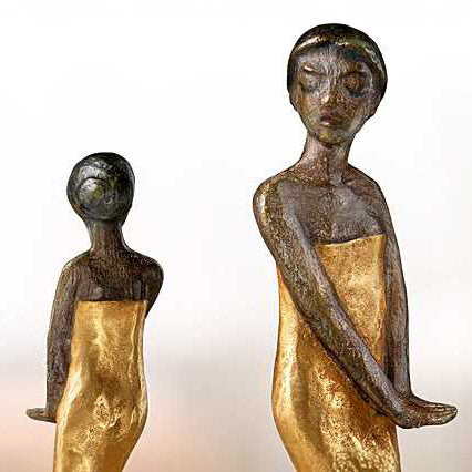 Zwei Skulpturen von Frauen mit goldfarbenen Kleidern, eine größere und eine kleinere, stehen nebeneinander.