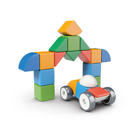 Bunte Bauklötze und ein Spielzeugauto mit weißen Rädern, das eine kleine Figur trägt, bilden eine Haus- oder Tor-Form.