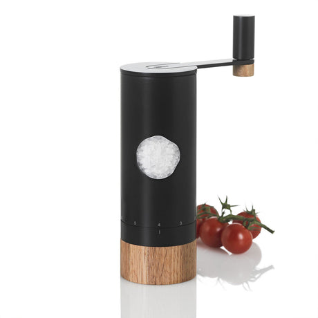 Salz- oder Pfeffermühle mit Holzbasis, schwarzem Gehäuse und Salz im Sichtfenster, neben Tomaten.