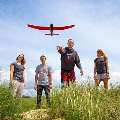 Vier Menschen stehen im Gras, einer wirft einen roten Drohnenflieger in die Luft. Es ist ein sonniger Tag.
