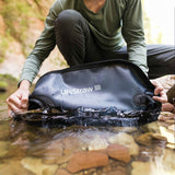 Person hält eine aufblasbare Wasserflasche mit Wasser im Fluss.