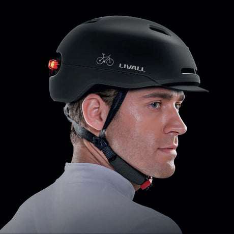 Mann trägt schwarzen Fahrradhelm mit LED-Licht, Blick nach rechts, schwarzer Hintergrund.