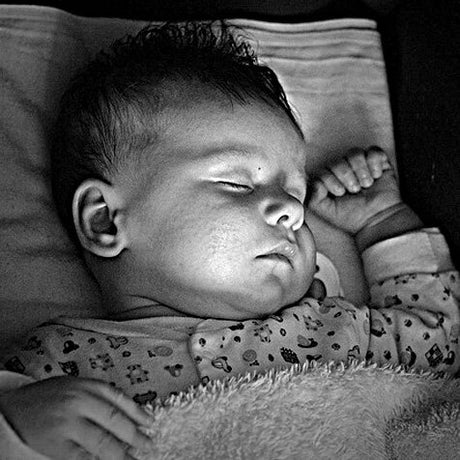 Neugeborenes Baby schläft auf einem Kissen, mit geschlossenen Augen und einer Hand am Kopf.