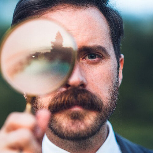 Mann mit Brille, Blick durch Lupenlinse, unscharfer Hintergrund, Nahaufnahme.