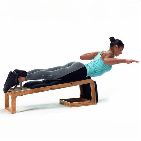 Frau liegt auf einem Pilates-Reformer, macht eine Rückenübung, trägt Sportkleidung, Haare im Dutt.