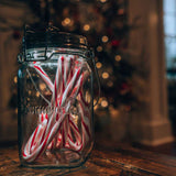 Glas mit roten und weißen Zuckerstangen vor einem Weihnachtsbaum im Hintergrund.
