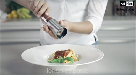 Person würzt Spaghetti mit Pfeffer über einem Teller Pasta.
