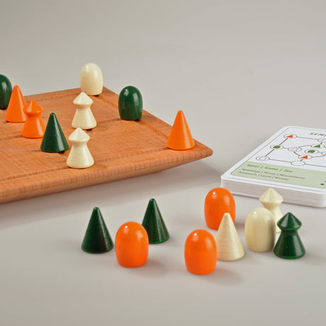 Holzschachbrett mit grünen, weißen und orangen Spielfiguren, daneben Spielanleitung.