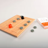 Holzbrett mit grauen Spielsteinen, einem schwarzen und einem roten Spielstein, Spielanleitung und Karten.