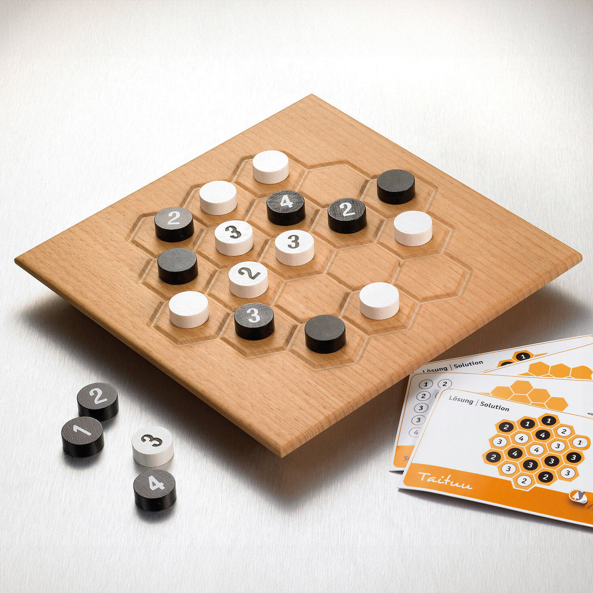 Holzbrettspiel mit schwarzen, weißen und grauen Spielsteinen, Spielanleitung liegt daneben.