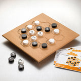 Holzbrettspiel mit schwarzen, weißen und grauen Spielsteinen, Spielanleitung liegt daneben.